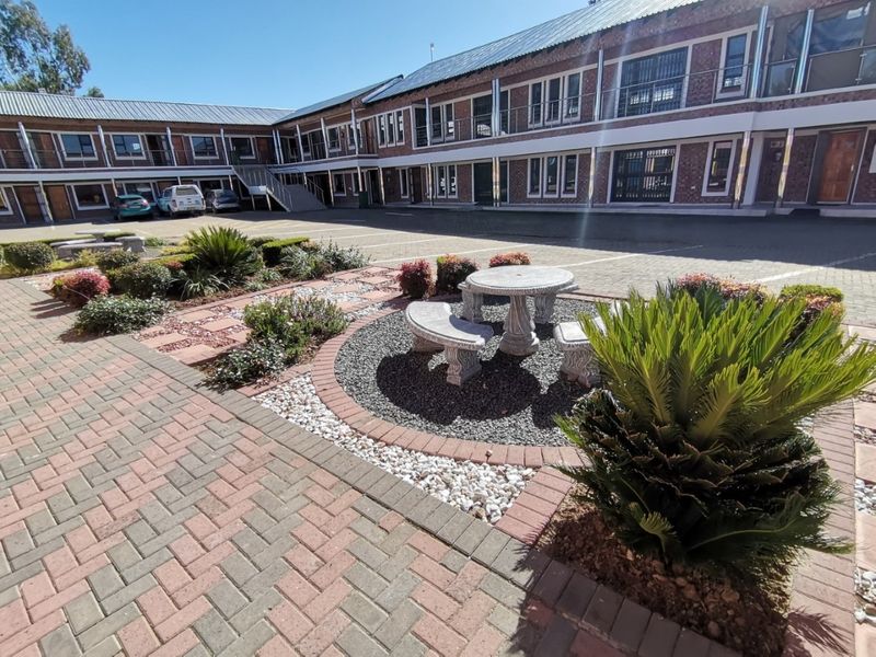 A well-maintained exterior courtyard featuring paved surfaces, brick building facades with balconies, and landscaped garden areas with stone seating.