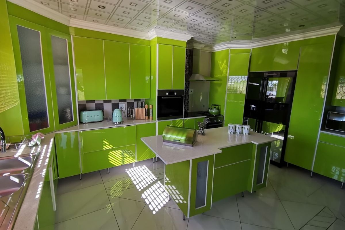 Modern kitchen featuring vibrant green high-gloss cabinetry, a central island with stone countertops, built-in oven, and decorative ceiling tiles.