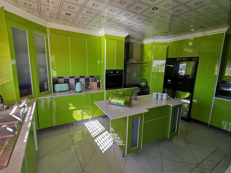Modern kitchen featuring vibrant green high-gloss cabinetry, a central island with stone countertops, built-in oven, and decorative ceiling tiles.