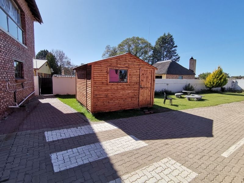 A view of the rear garden area featuring a wooden storage shed, paved driveway, and surrounding boundary walls on the small holding property.