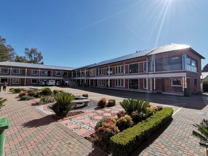 A well-maintained multi-story brick building with a paved courtyard, landscaped garden beds, and solar panels installed on the metal roof.