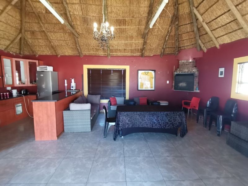 Open-plan living area featuring a thatched roof with exposed rafters, a built-in brick fireplace, and a functional kitchen with granite countertops.