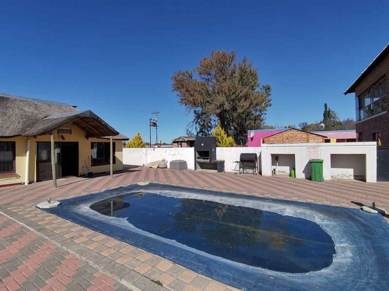 Outdoor pool area featuring a paved patio, built-in braai, and a covered swimming pool, set within a walled garden space.