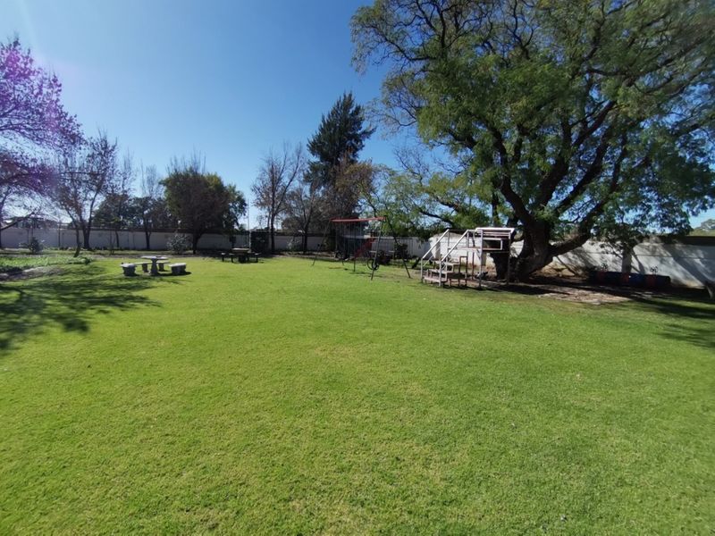 A spacious, well-maintained garden area featuring a large lawn, mature trees, and a perimeter wall, providing an open outdoor space.