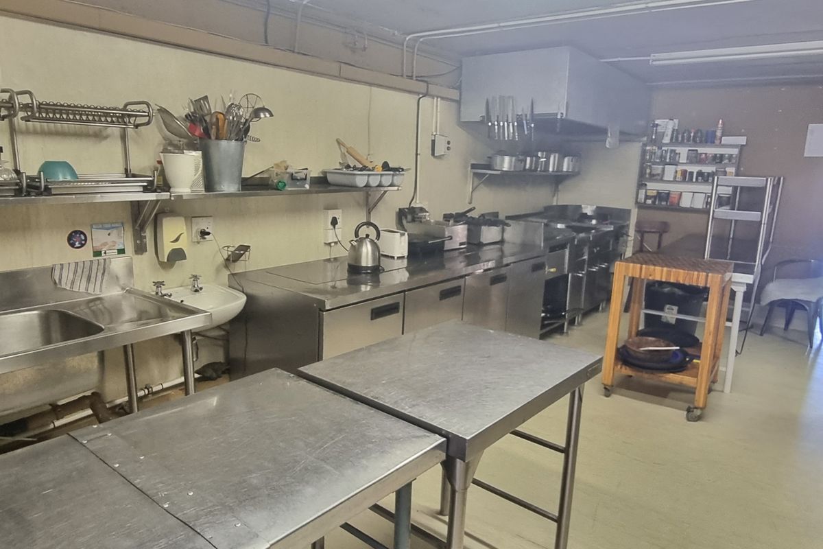 A functional commercial-style kitchen featuring stainless steel work surfaces, integrated sinks, and professional-grade extractor fan system.