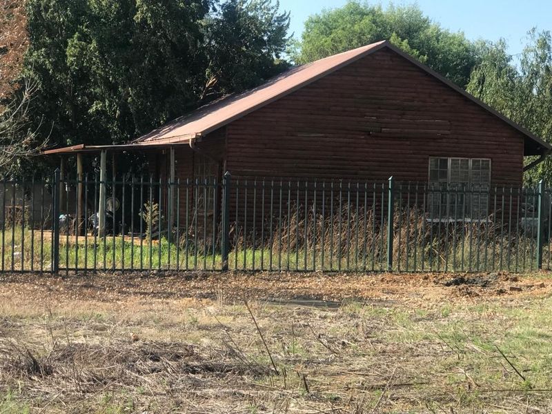 A rustic log cabin structure featuring a metal roof and covered patio, enclosed by steel palisade fencing on a large plot.
