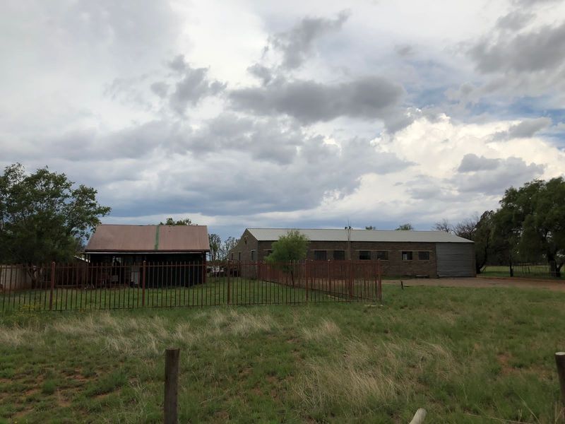 View of the rear exterior of the small holding, featuring multiple outbuildings with corrugated metal roofing and secure steel palisade fencing.