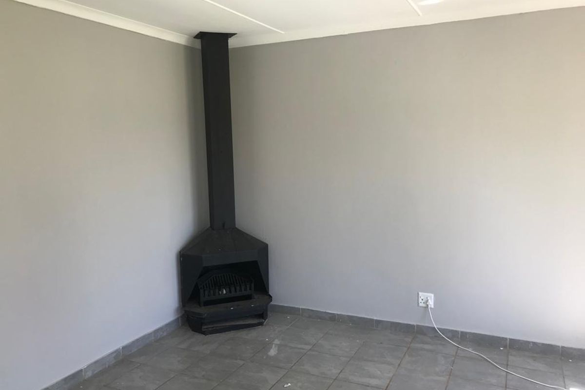 An empty living room featuring a corner fireplace, tiled flooring, and neutral grey walls, offering a blank canvas for interior design.