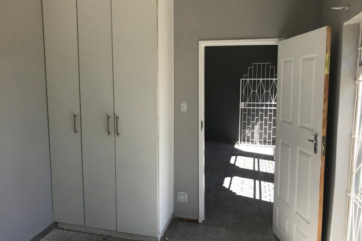 A vacant bedroom featuring built-in cupboards, tiled flooring, and a security gate, currently requiring minor finishing touches to the flooring and walls.