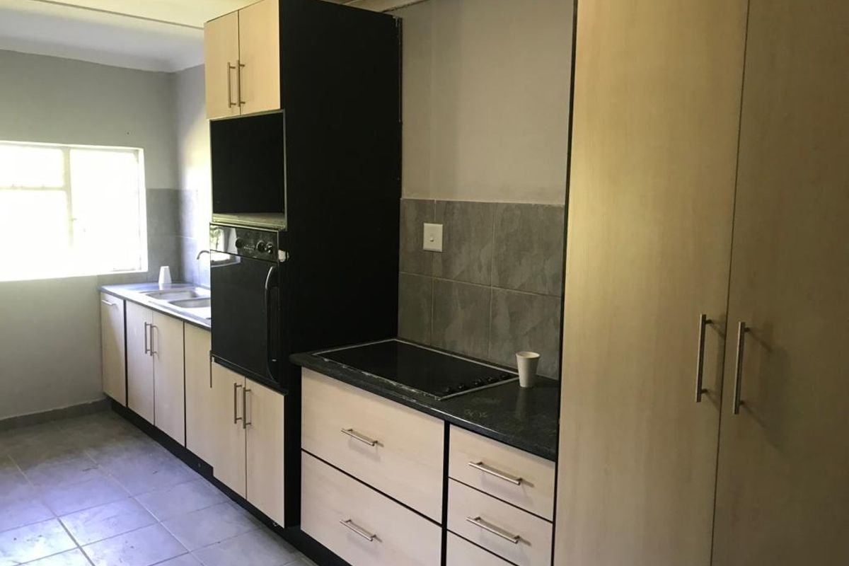 A functional kitchen featuring built-in cabinetry, a dark laminate countertop, integrated oven and hob, and tiled flooring with a neutral backsplash.