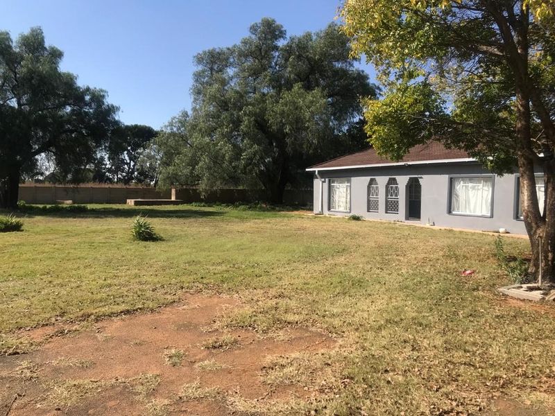 A view of the rear garden and property elevation, featuring a spacious lawn, mature trees, and a perimeter wall.