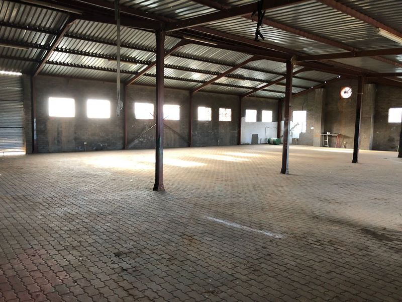 A large, open-plan industrial utility space featuring a steel portal frame, corrugated metal roofing, and durable paved flooring, suitable for storage or workshop use.