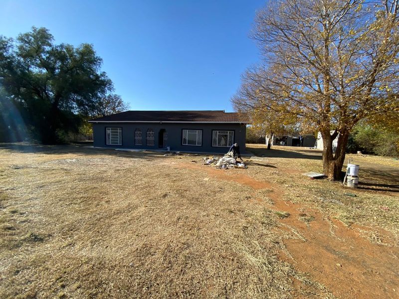 Front elevation of a single-story residential dwelling featuring a tiled roof and security-fitted windows, set on a large open plot.