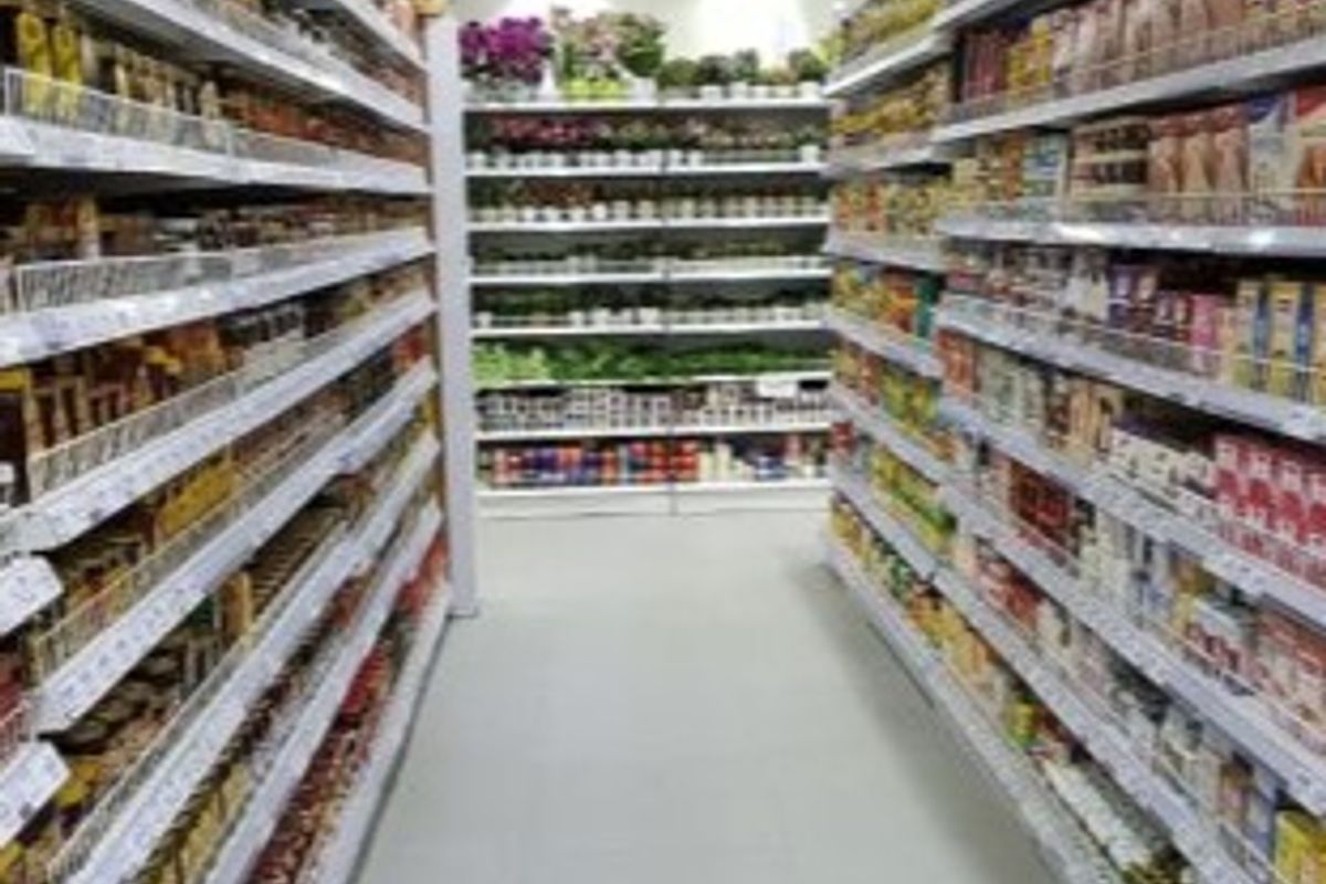A retail aisle featuring multiple rows of fixed shelving units stocked with various products under bright recessed ceiling lighting.