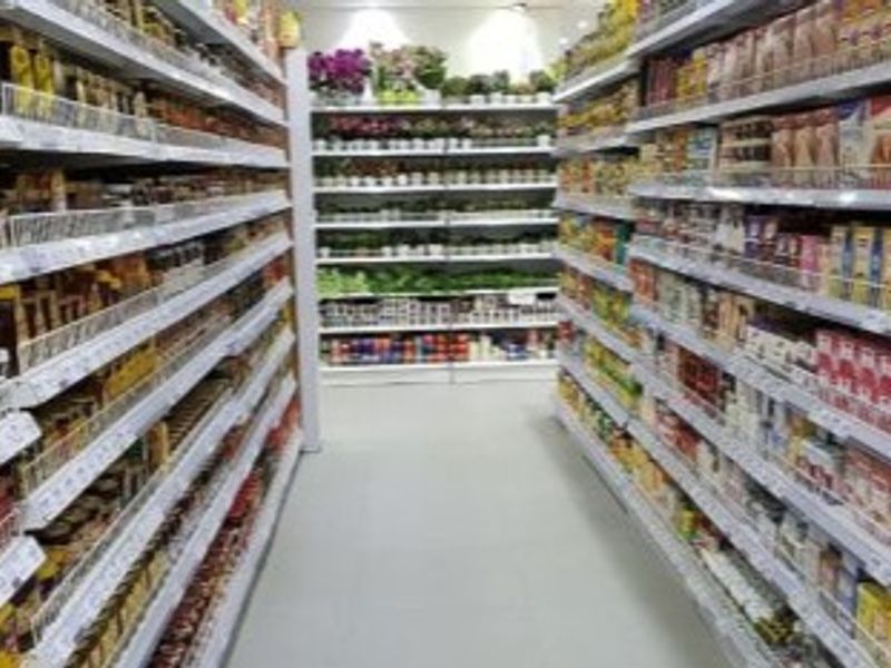 A retail aisle featuring multiple rows of fixed shelving units stocked with various products under bright recessed ceiling lighting.