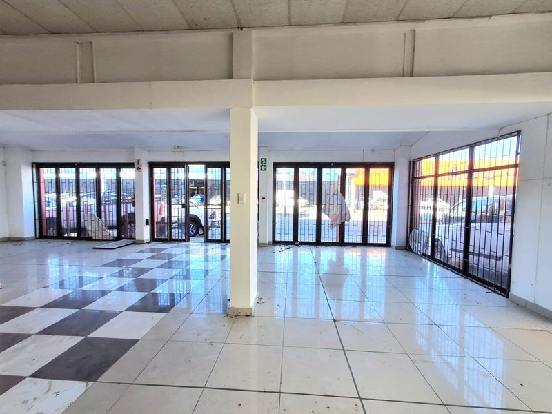 Spacious open-plan commercial unit featuring large glass storefronts with security gates, tiled flooring, and exposed structural beams, suitable for retail or office use.