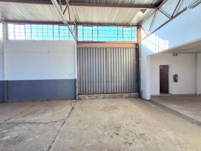 Spacious industrial utility area featuring high ceilings with exposed steel trusses, large metal roller shutter door, and durable concrete flooring.