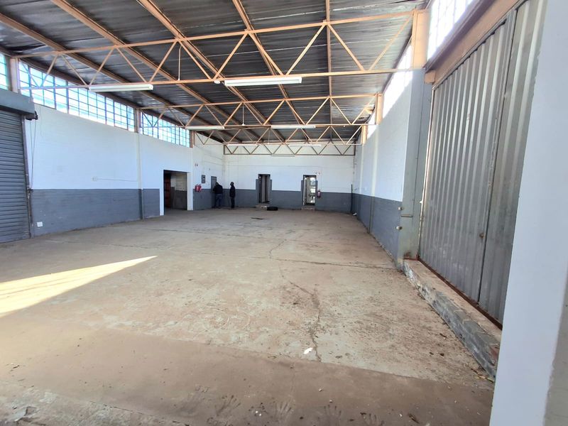 Spacious industrial utility area featuring exposed steel roof trusses, concrete flooring, and a large roller shutter door, suitable for storage or workshop use.