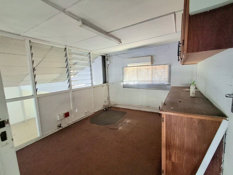 An empty office space featuring louvre windows, built-in cabinetry, and a split-system air conditioner, requiring cosmetic updates to improve its condition.