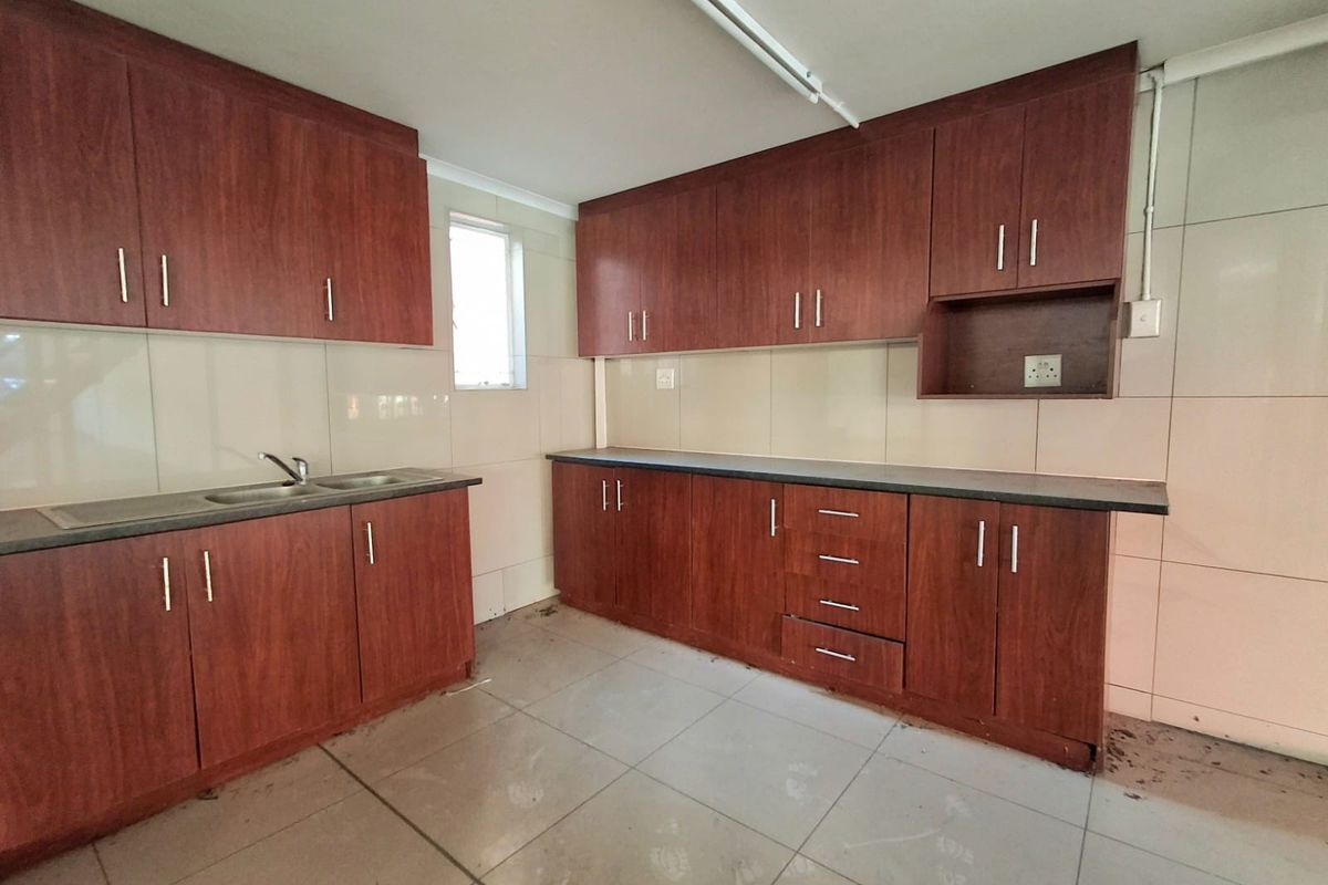 A functional kitchen space featuring wood-look laminate cabinetry, ample counter space, a stainless steel sink, and tiled finishes throughout.