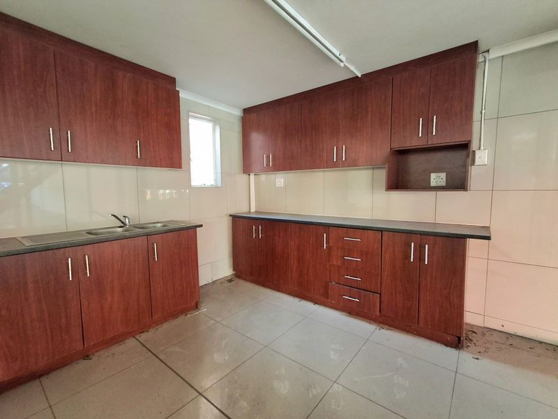 A functional kitchen space featuring wood-look laminate cabinetry, ample counter space, a stainless steel sink, and tiled finishes throughout.