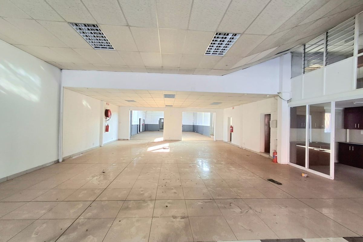 Spacious open-plan commercial area featuring tiled flooring, suspended ceilings with recessed lighting, and a glass-partitioned office or storage section.