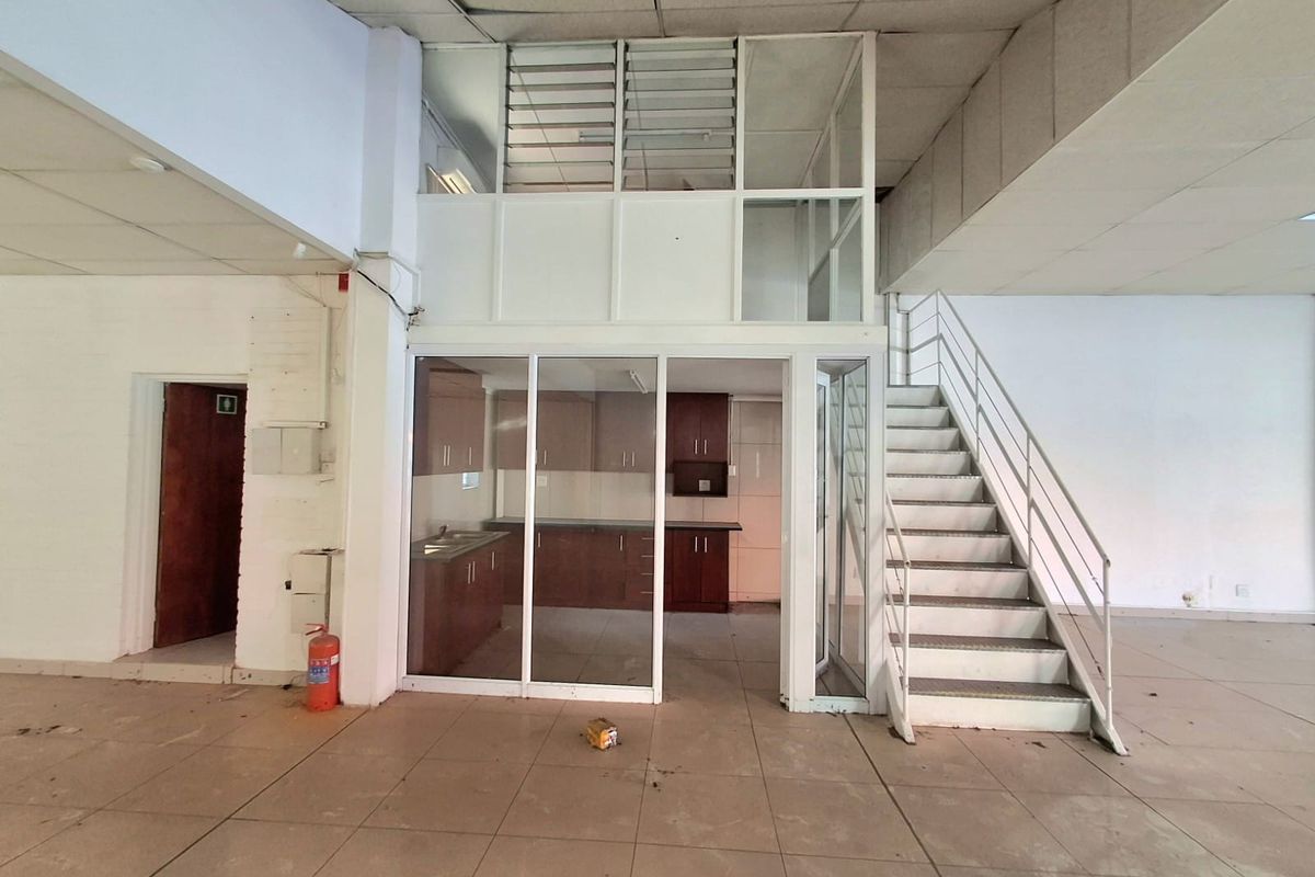 Open plan commercial space featuring a metal staircase, glass-enclosed kitchen area, and suspended ceiling, offering a versatile layout for business operations.