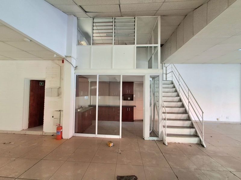 Open plan commercial space featuring a metal staircase, glass-enclosed kitchen area, and suspended ceiling, offering a versatile layout for business operations.