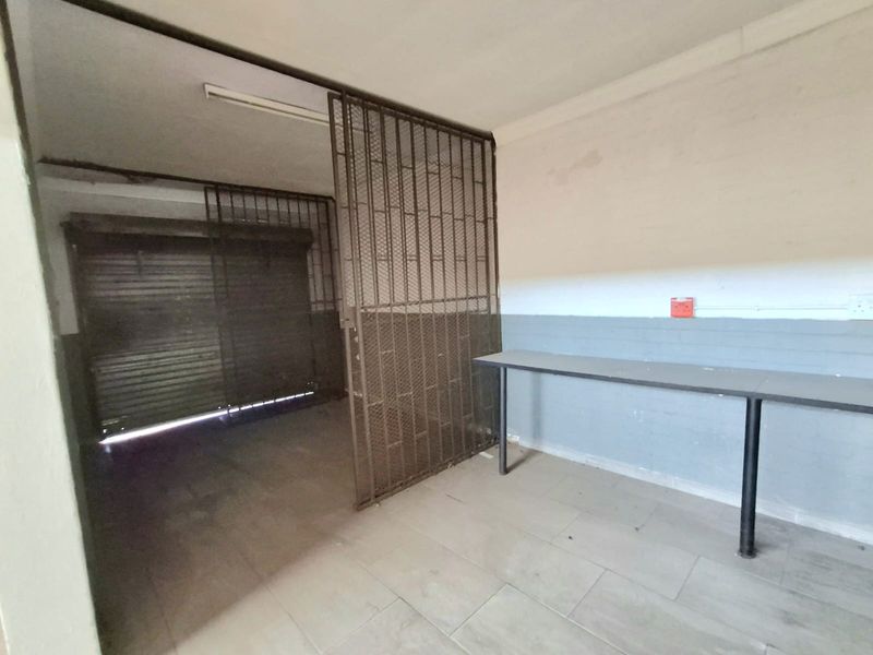 A functional utility or storage area featuring a secure metal gate, roller shutter door, tiled flooring, and a built-in workbench.