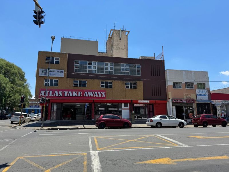 Street-level view of a multi-story commercial building featuring a prominent storefront with signage and security bars on the upper levels.