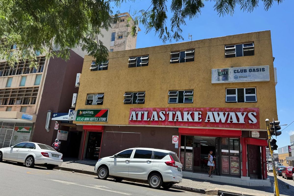 Street-level view of a multi-story commercial building featuring ground-floor retail units, including a takeaway and bottle store, with prominent signage.