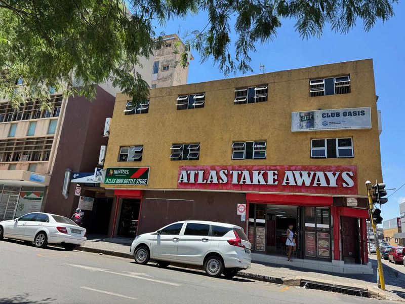 Street-level view of a multi-story commercial building featuring ground-floor retail units, including a takeaway and bottle store, with prominent signage.