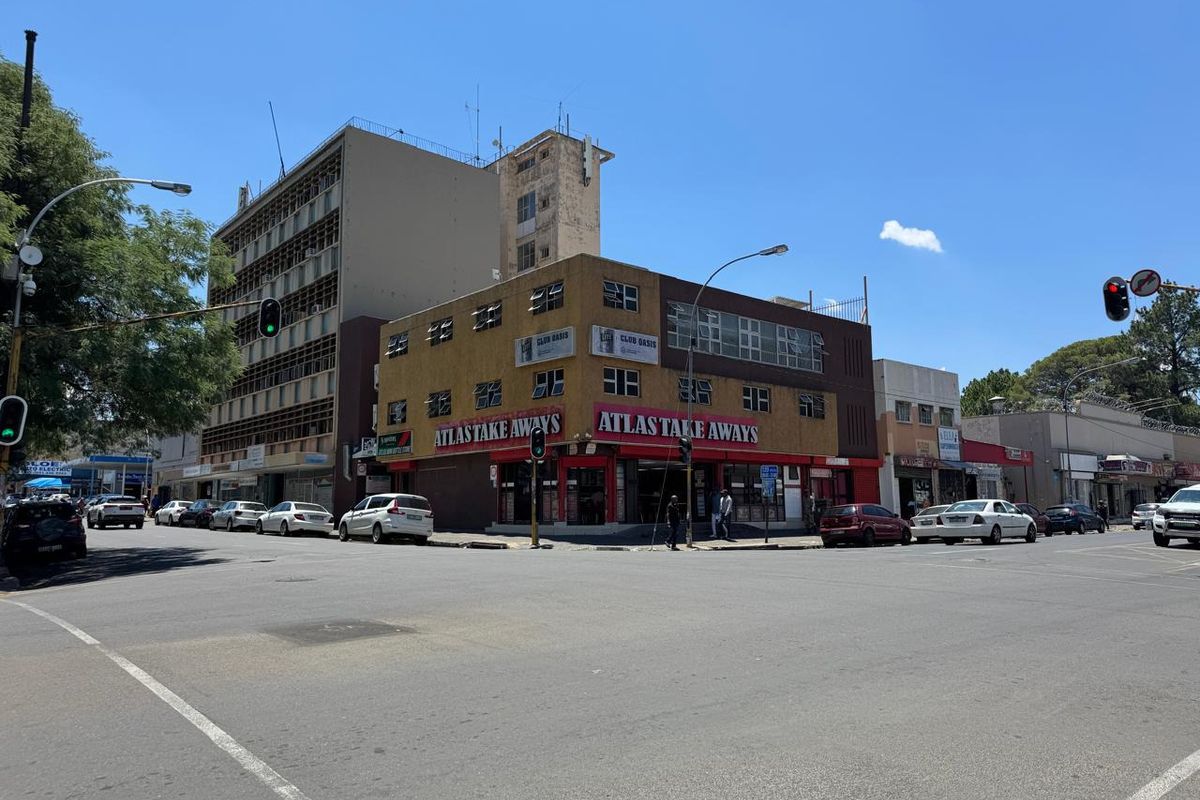 A corner commercial building featuring street-level retail space and upper-level windows, situated at a busy urban intersection.