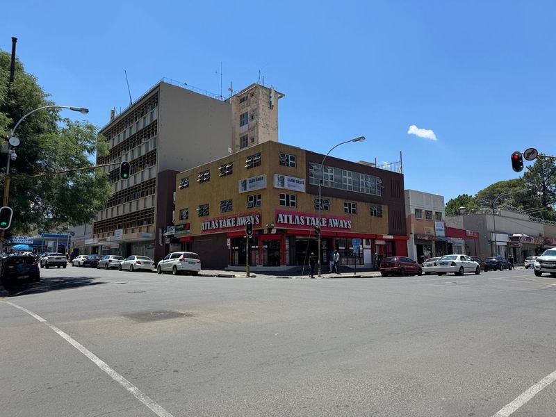 A corner commercial building featuring street-level retail space and upper-level windows, situated at a busy urban intersection.