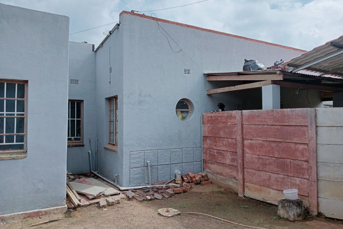 Rear exterior view of the commercial property showing a grey rendered facade, circular window, and a precast concrete boundary wall with an attached lean-to structure.