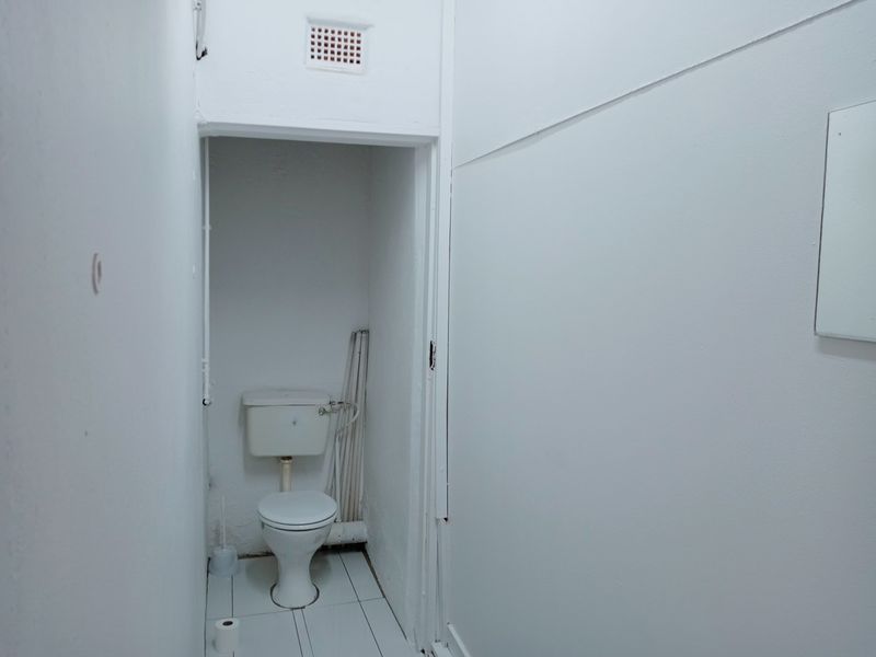 A compact, functional bathroom featuring a standard toilet, tiled flooring, and wall-mounted ventilation, currently in need of cosmetic updates.