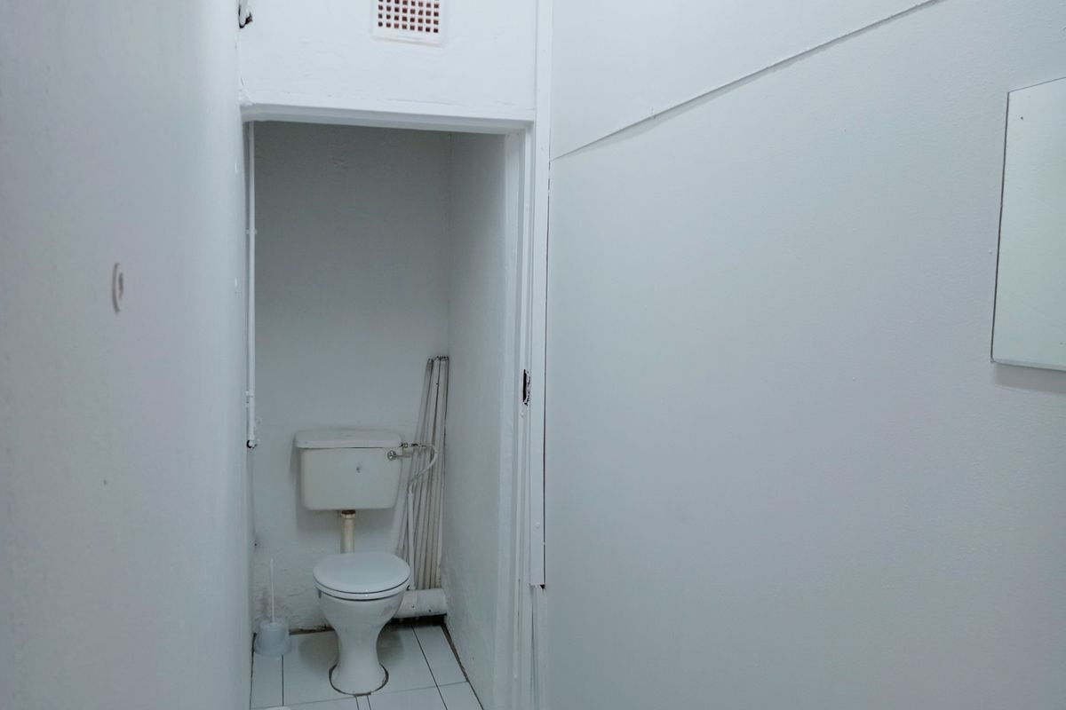 A compact, functional bathroom featuring a standard toilet, tiled flooring, and wall-mounted ventilation, currently in need of cosmetic updates.
