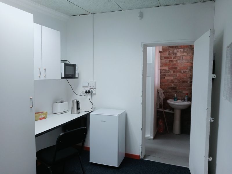 A compact kitchenette area featuring built-in cabinetry and a countertop, with an adjacent small washroom area containing a pedestal sink.
