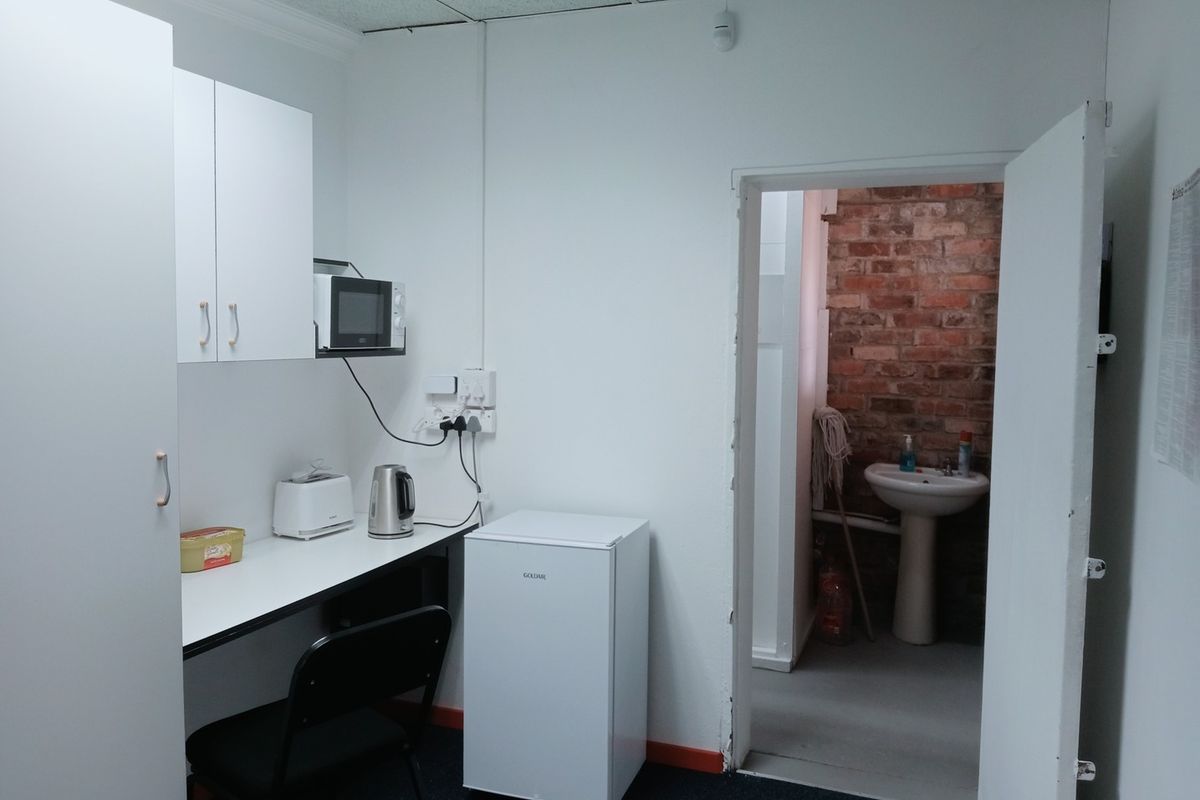 A compact kitchenette area featuring built-in cabinetry and a countertop, with an adjacent small washroom area containing a pedestal sink.