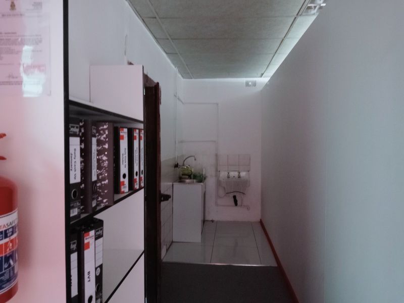 A functional utility or scullery area featuring a stainless steel sink, tiled flooring, and exposed plumbing fixtures in a commercial setting.