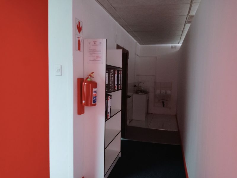 A commercial hallway featuring a fire extinguisher, drop ceiling, and a small utility sink area at the end of the corridor.