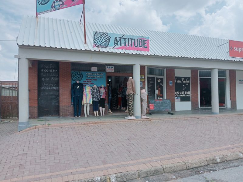 Front elevation of a commercial retail unit featuring a brick facade, corrugated metal roof, and covered walkway with concrete support columns.