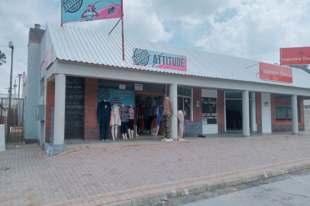 Commercial storefront featuring a corrugated metal roof, brick facade, and concrete pillars, located along a paved sidewalk with multiple business signs.