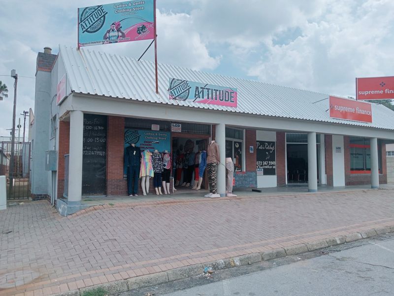 Commercial storefront featuring a corrugated metal roof, brick facade, and concrete pillars, located along a paved sidewalk with multiple business signs.