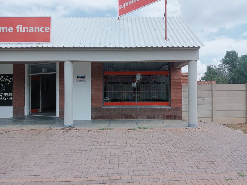 Front facade of a commercial property featuring brickwork, concrete columns, large display windows, and a paved entrance area.