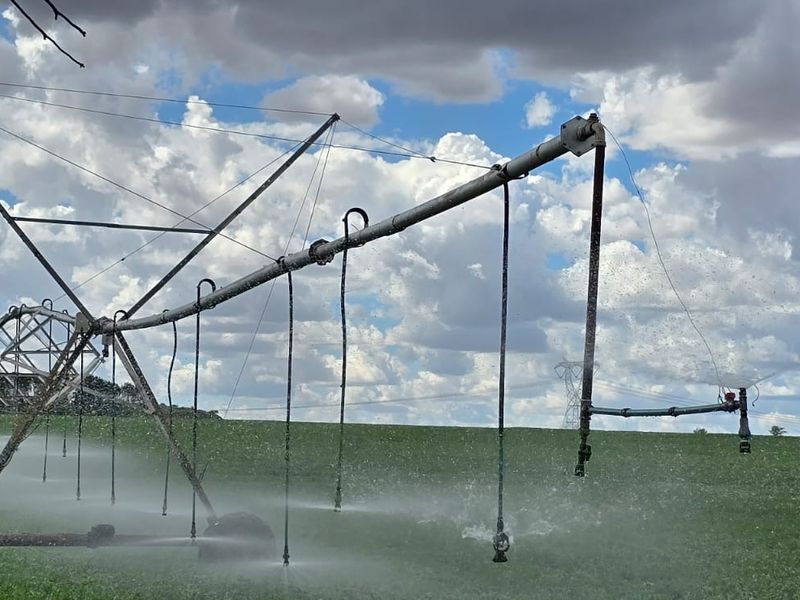 A large-scale center pivot irrigation system operating in a green agricultural field under a cloudy sky.
