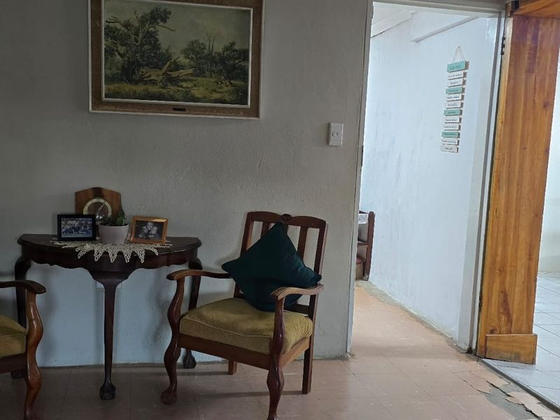 A living area featuring tiled flooring and a wooden door frame leading to an adjacent room, showing signs of wear on the floor and walls.
