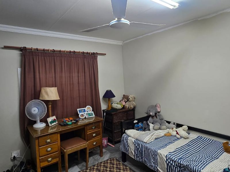 A functional bedroom featuring a ceiling fan, neutral wall finishes, and a curtain rod, providing a practical space for rest.