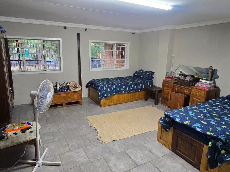 Spacious bedroom featuring tiled flooring, large windows with security bars, and functional overhead lighting.