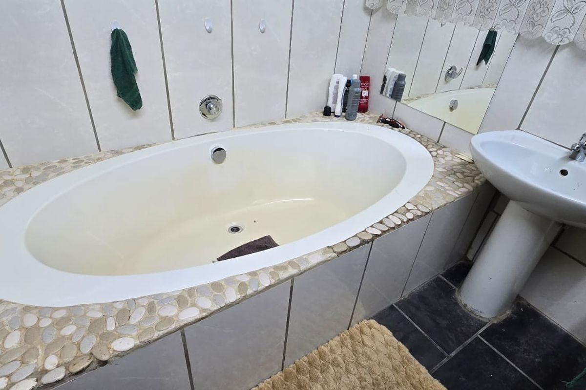 A bathroom featuring a built-in oval bathtub with a decorative pebble-style surround and a classic pedestal washbasin.